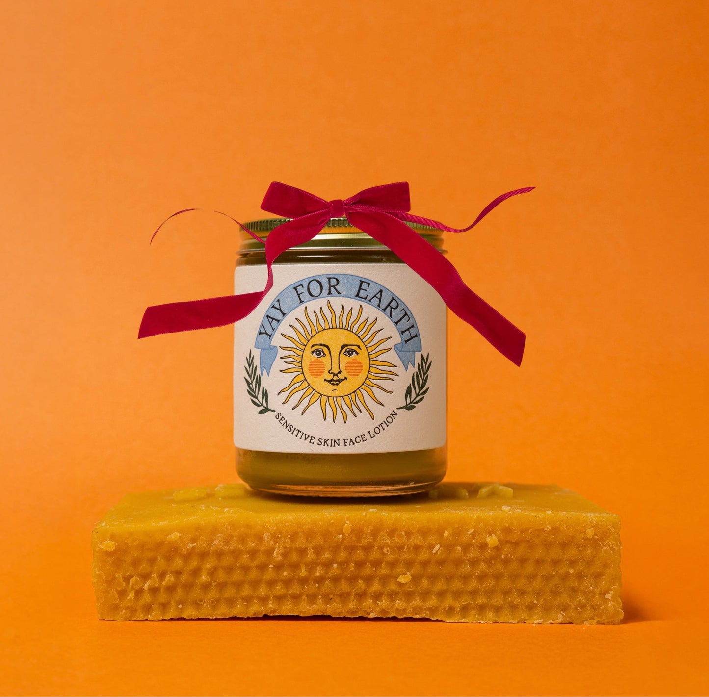 Jar of 'Pay for Earth' product on a honeycomb block with a red ribbon against an orange background