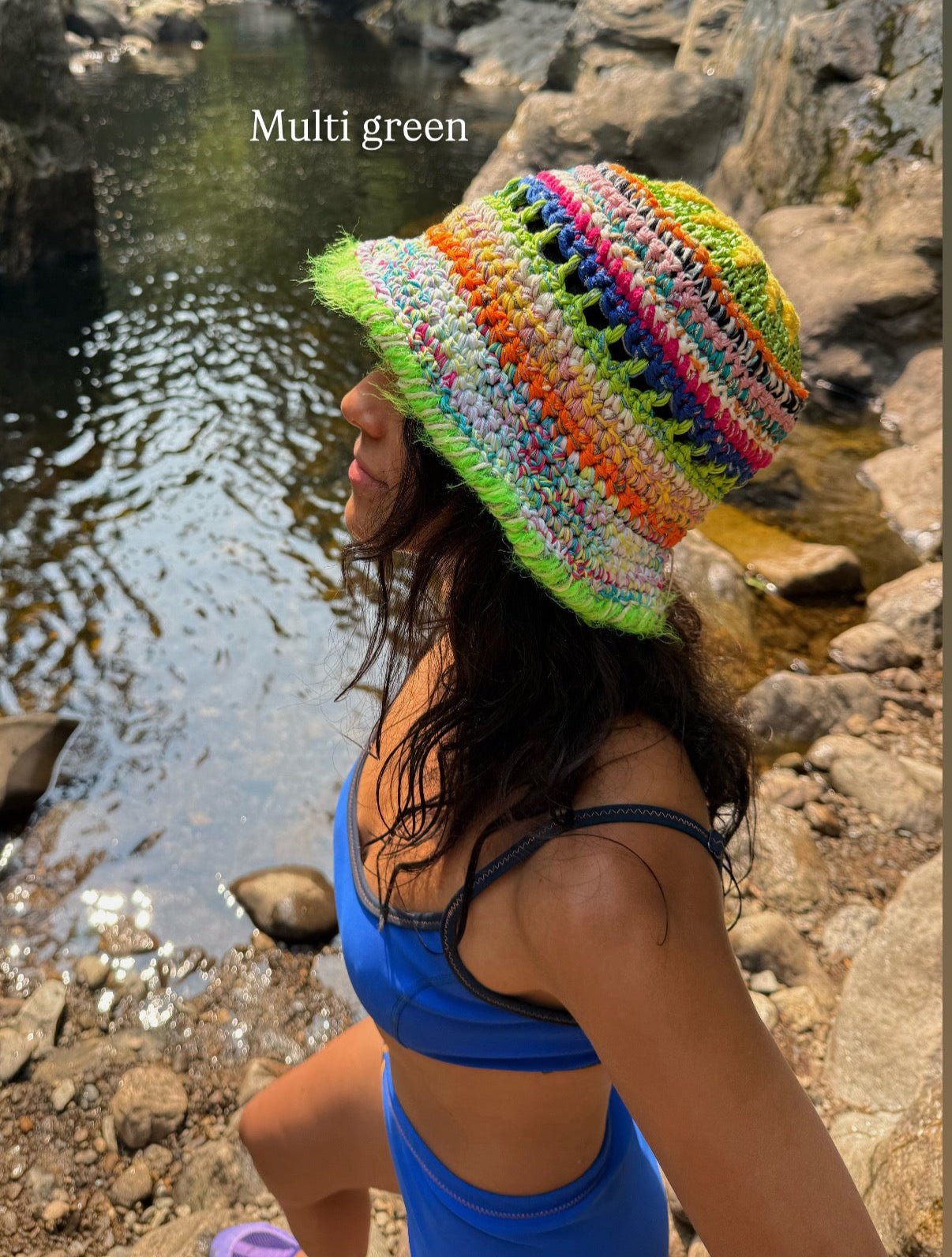 Person wearing a colorful knit hat by a stream with 'Multi green' text overlay