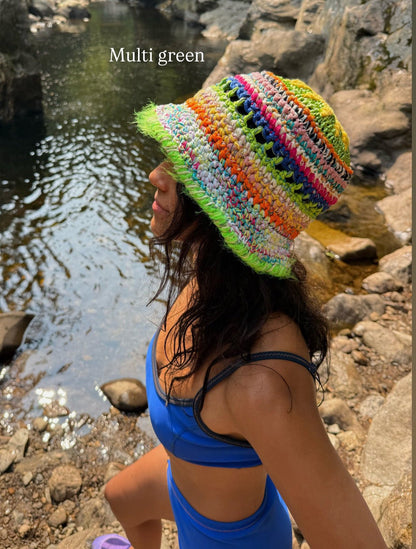 Person wearing a colorful knit hat by a stream with 'Multi green' text overlay